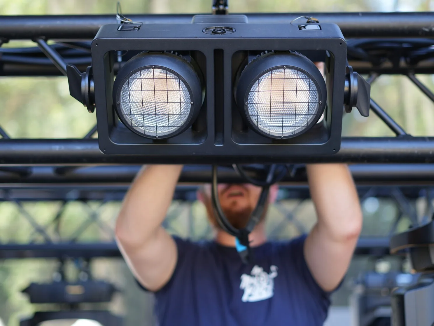 Montage et réglage d'un blinder Strike Array sur un pont lumière par un technicien pour un festival.