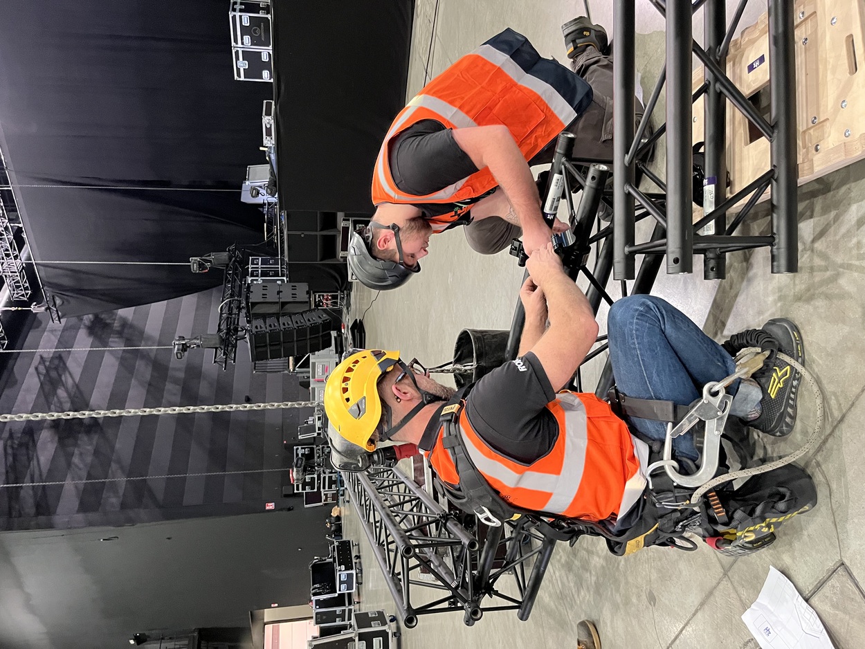 Techniciens rigg en pleine installation d'un pont lumière en structure noire.